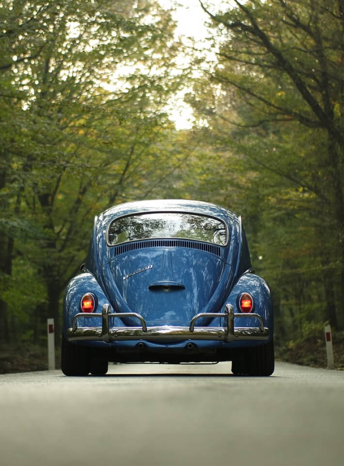 オープンカーに乗ったカップルが夕日を眺めながらドライブし、女性が両手を上げている後ろ姿