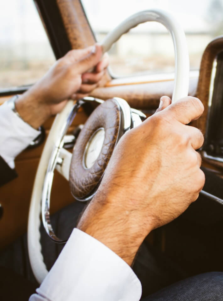 自然豊かな山道で、赤いオープンカーにもたれかかる女性が遠くを見つめている