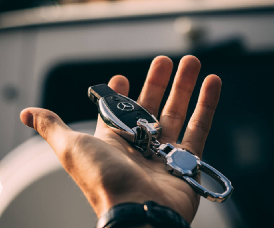 車のキーとキーチェーンを手に持っている様子。メルセデス・ベンツのブランドロゴが確認できる高級車のキー