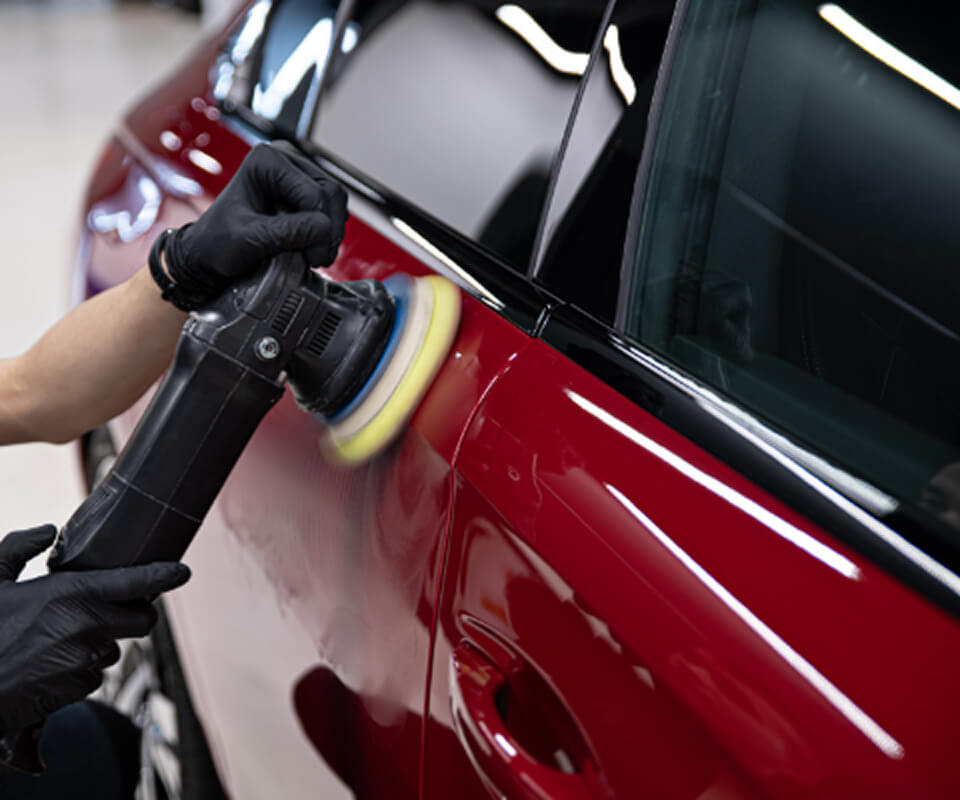 車の研磨作業の場面。専門的な研磨機を使って車の塗装面を美しく仕上げている様子で、自動車美容の専門作業