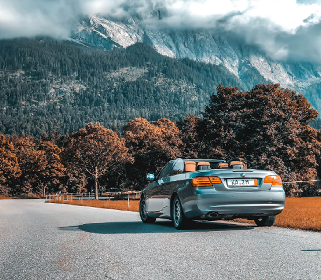 山々と雲に囲まれた自然の中、オープンカーが静かに道路脇に停まっている風景